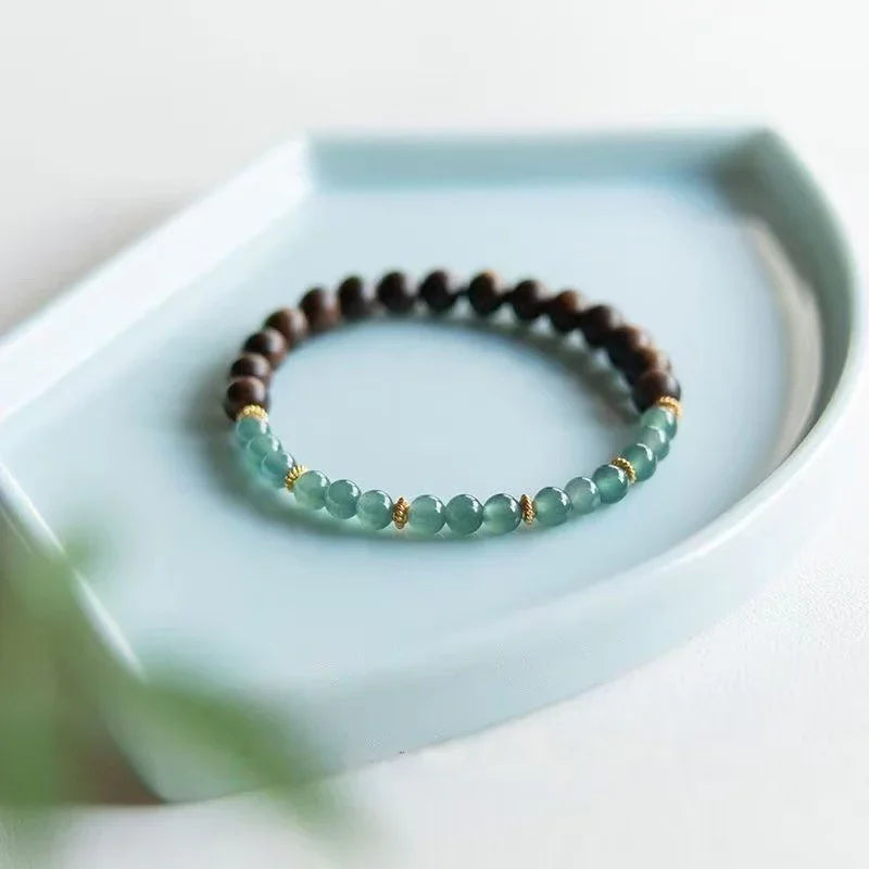 Beaded bracelet with brown and green beads accented by gold spacers on a light blue ceramic tray