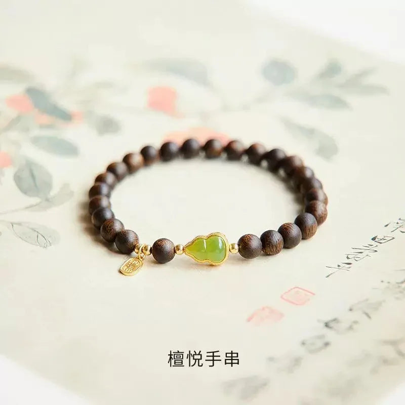Brown wooden bead bracelet with central green jade gourd charm and gold accents on paper background