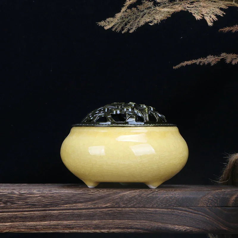 Yellow ceramic incense burner with intricate dark lid on wooden surface against black background
