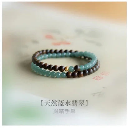 Natural blue-green jade and dark wooden bead bracelet with golden accent on light background