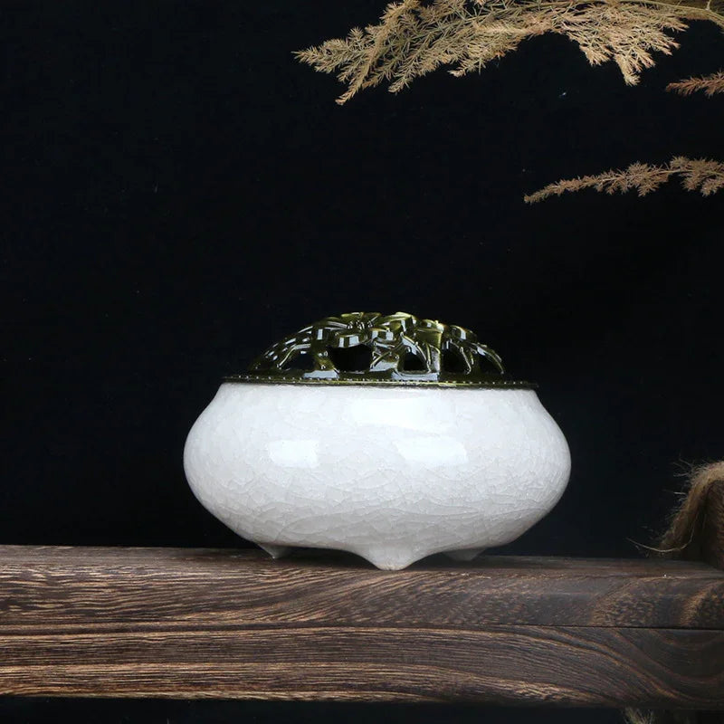 White ceramic incense burner with intricate green carved lid on wooden surface against black background