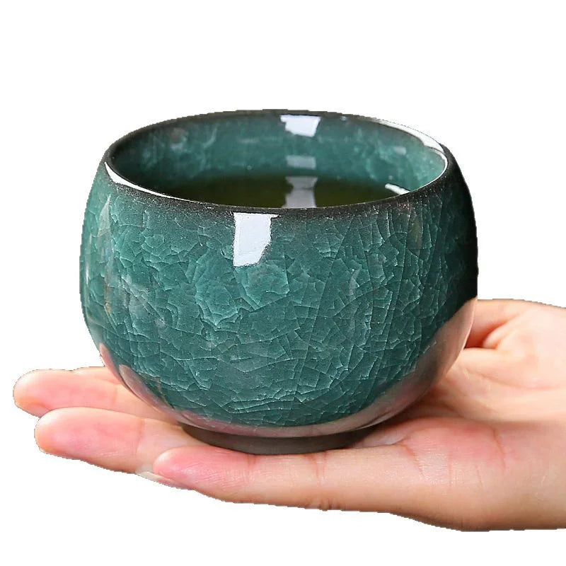 Hand holding a textured green ceramic tea cup filled with tea on white background
