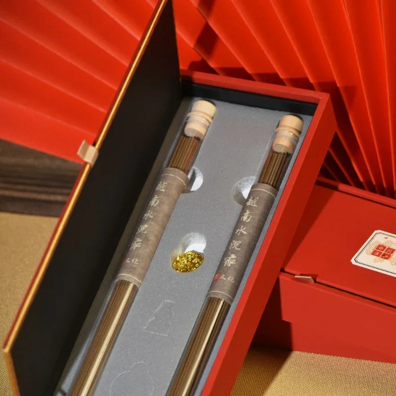 Open red gift box with two glass tubes of incense sticks and golden beads inside a gray foam insert