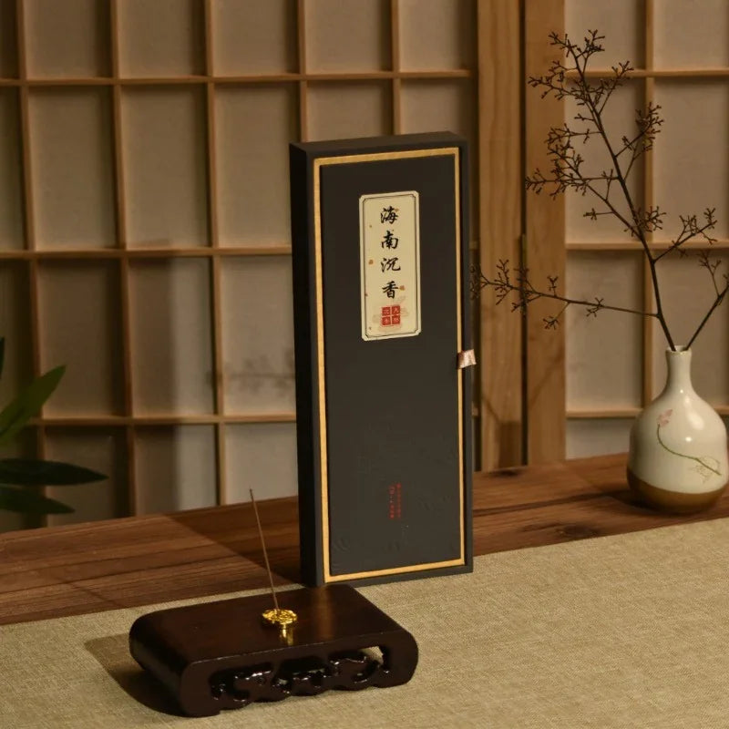 Black incense box with Chinese characters, wooden incense holder with burning stick, vase with dried branches on wooden table