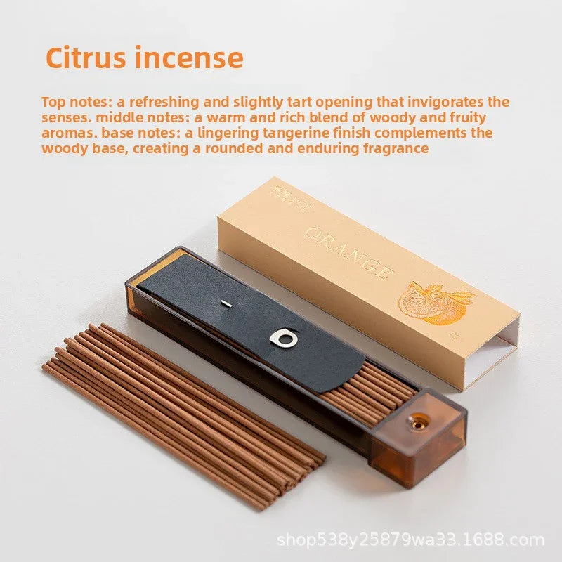 Citrus incense sticks with orange-scented packaging and black holder on white surface