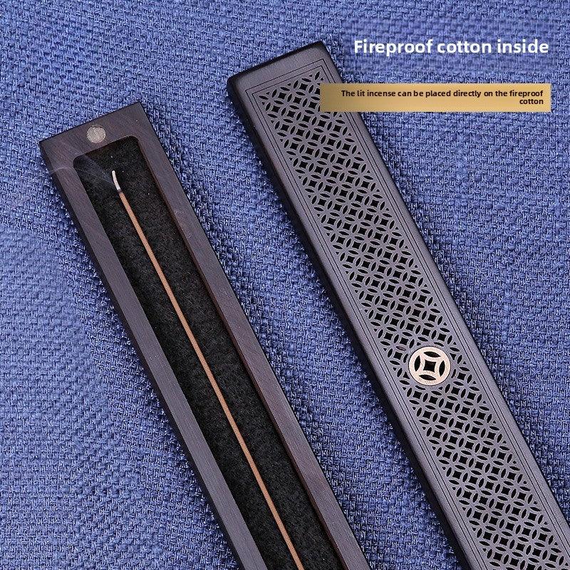 Decorative black incense holder with fireproof cotton and lit incense stick on blue fabric