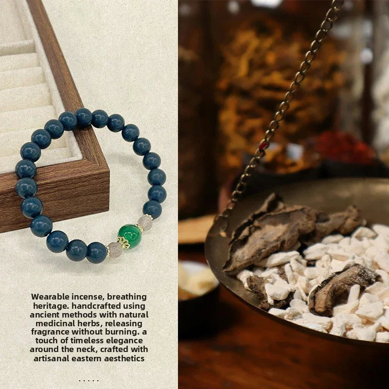 Blue beaded wrist mala bracelet with green and clear beads on a beige surface next to wooden jewelry box